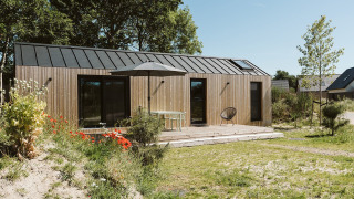 Casa pequeña de madera moderna con terraza y sombrilla en De Klepperstee, Países Bajos, rodeada de naturaleza.