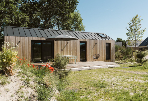 Casa pequeña de madera moderna con terraza y sombrilla en De Klepperstee, Países Bajos, rodeada de naturaleza.