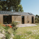 Moderne træ tiny house med sort tag, terrasse og parasol, omgivet af natur ved De Klepperstee, Holland.