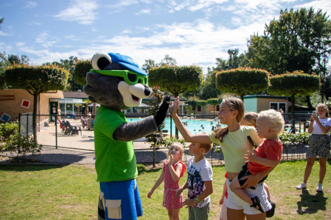 Kinder und Erwachsene geben einem Maskottchen im Ferienpark mit Pool in Gelderland, Niederlande, High-Five.
