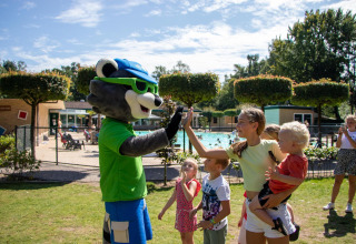 Kinder und Erwachsene geben einem Maskottchen im Ferienpark mit Pool in Gelderland, Niederlande, High-Five.