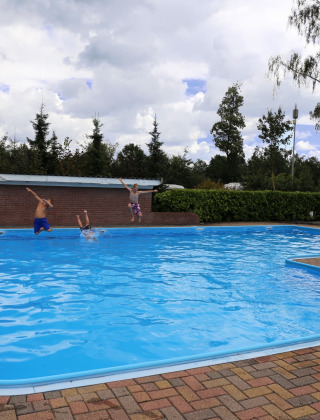 Niños saltan a la piscina al aire libre en Camping de Meibeek, un parque de vacaciones en Gelderland, Países Bajos.