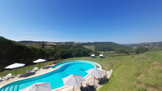 Buitenzwembad met ligstoelen en parasols en uitzicht op heuvels bij Casa & Glamping Sorriso in Umbrië, Italië.