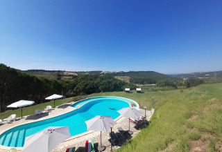 Buitenzwembad met ligstoelen en parasols en uitzicht op heuvels bij Casa & Glamping Sorriso in Umbrië, Italië.