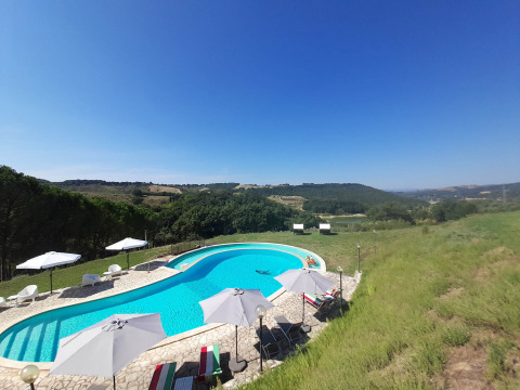 Outdoor pool with lounge chairs and umbrellas overlooking rolling hills at Casa & Glamping Sorriso in Umbria, Italy.