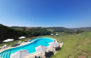 Buitenzwembad met ligstoelen en parasols en uitzicht op heuvels bij Casa & Glamping Sorriso in Umbrië, Italië.
