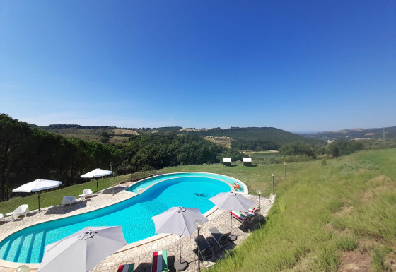 Outdoor pool with lounge chairs and umbrellas overlooking rolling hills at Casa & Glamping Sorriso in Umbria, Italy.