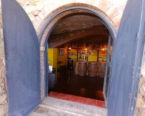 Arched doorway opens to a cozy wine bar with barrels at Casa & Glamping Sorriso, Umbria, Italy.