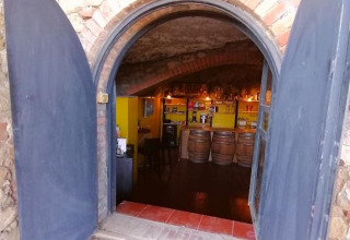 Blick durch gewölbte Eingangstür in einen Weinkeller mit Bar und Fässern in Casa & Glamping Sorriso.