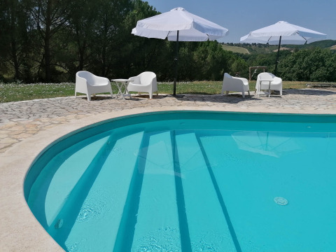 Piscine extérieure avec chaises blanches et parasols à Casa & Glamping Sorriso, en Ombrie, Italie.