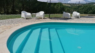 Piscina al aire libre con sillas y sombrillas blancas en Casa & Glamping Sorriso, en Umbría, Italia.