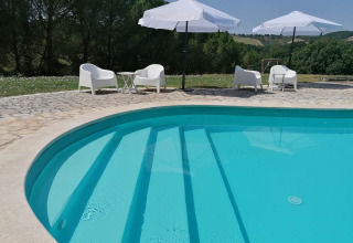 Piscine extérieure avec chaises blanches et parasols à Casa & Glamping Sorriso, en Ombrie, Italie.