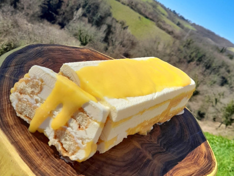Porción de postre con crema de limón sobre tabla de madera, colinas de Umbría, Italia al fondo.