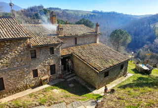 Stenen huis aan Casa & Glamping Sorriso, Umbrië, Italië, met heuvels en natuur op de achtergrond.