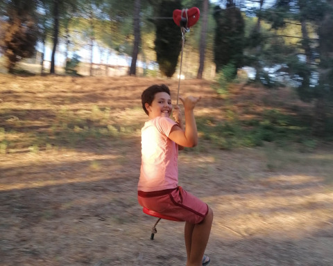Child smiling and riding a zipline outdoors at Casa & Glamping Sorriso holiday park in Umbria, Italy.