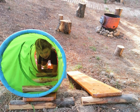Kind kruipt door een groene tunnel op de buitenspeelplaats van Casa & Glamping Sorriso in Umbrië, Italië.