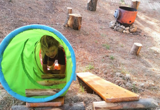 Barn leger i grøn tunnel på legeplads udenfor ved Casa & Glamping Sorriso i Umbrien, Italien, med brænde og træstubbe.