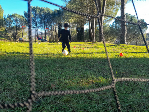 Un niño juega al fútbol en un campo verde de Casa & Glamping Sorriso, rodeado de árboles en Umbría, Italia.