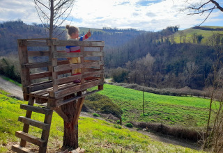 A child stands in a treehouse overlooking hills and fields at Casa & Glamping Sorriso in Umbria, Italy.