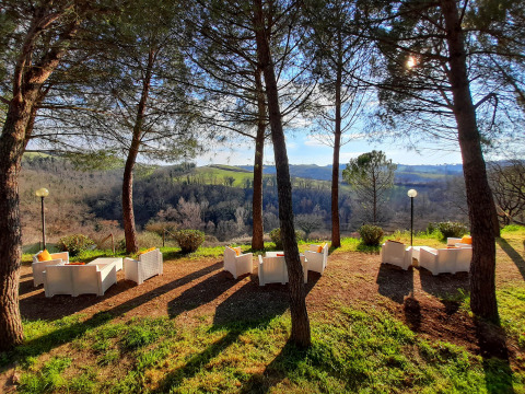 Buitenstoelen onder bomen met uitzicht op glooiende heuvels bij Casa & Glamping Sorriso in Umbrië, Italië.