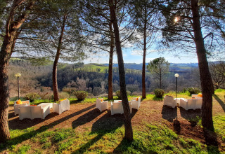 Udendørs loungestole under træer med udsigt over grønne bakker på Casa & Glamping Sorriso i Umbrien, Italien.