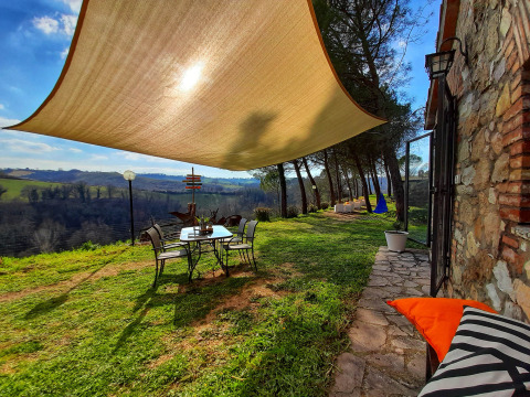 Tuinterras met schaduwdoek en uitzicht op de velden bij Casa & Glamping Sorriso, Umbrië, Italië.
