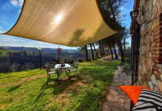 Tuinterras met schaduwdoek en uitzicht op de velden bij Casa & Glamping Sorriso, Umbrië, Italië.