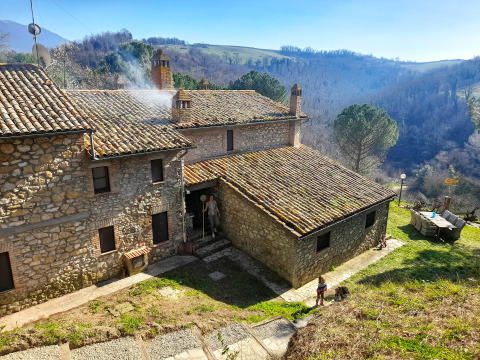 Casa de piedra con techo de tejas en Umbría, Italia, rodeada de colinas y naturaleza bajo el sol brillando.