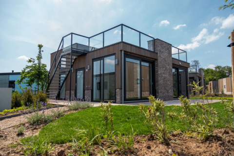 Moderne glamping accommodatie op een vakantiepark met glazen balustrade, buitentrap en aangelegde tuin