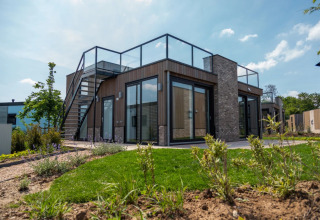 Modernes Glamping-Ferienhaus im Ferienpark mit Glasgeländer, Außentreppe und gepflegtem Garten