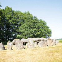 Oldtidsstenformation i grønt område nær feriepark, ideel til glamping og naturoplevelser.