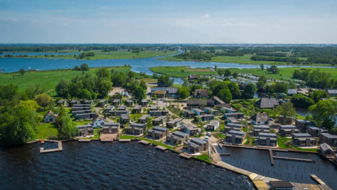 Vista aérea de un parque vacacional con alojamientos glamping junto al lago y rodeado de paisaje verde.