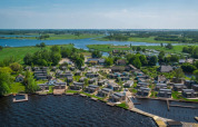 Vista aérea de un parque vacacional con alojamientos glamping junto al lago y rodeado de paisaje verde.
