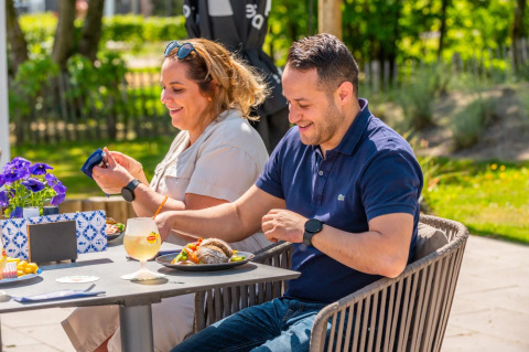 Couple enjoying a meal outdoors at a holiday park with glamping accommodations, surrounded by greenery.