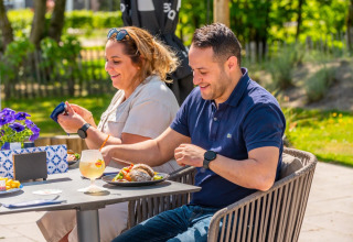 Couple dégustant un repas en plein air dans un parc de vacances avec glamping, entouré de verdure.