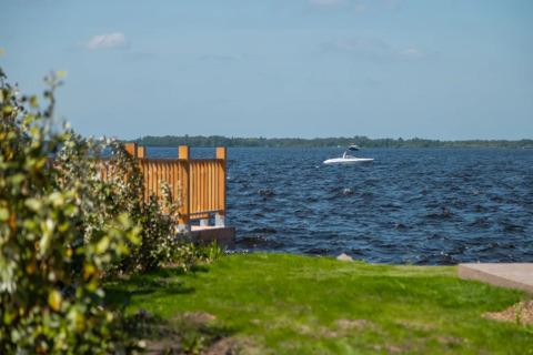 Blick auf einen See von einem Ferienpark mit Glamping, grüne Wiese, Holzzaun und Boot auf dem Wasser.