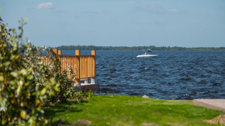 Udsigt over søen fra et feriepark med glamping, grønne plæner, træhegn og en båd på vandet.