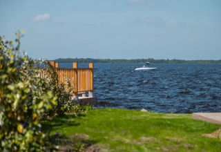 Blick auf einen See von einem Ferienpark mit Glamping, grüne Wiese, Holzzaun und Boot auf dem Wasser.