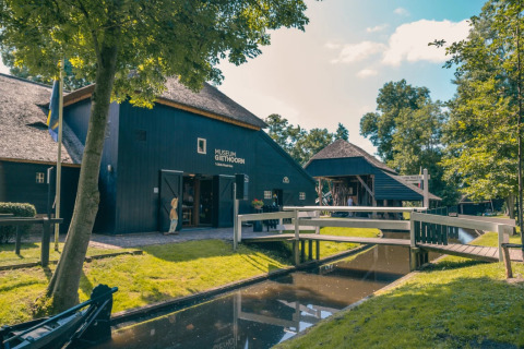 Foto des Museums Giethoorn in den Niederlanden mit Kanal, Fußgängerbrücke und üppigem Grün.