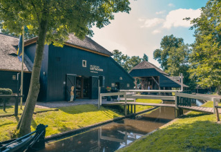 Billede af Museum Giethoorn i Holland, omgivet af grønne træer, en kanal og en malerisk bro.