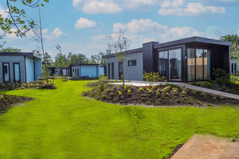 Cabañas modernas de glamping en un parque vacacional, rodeadas de césped verde y jardines cuidados.
