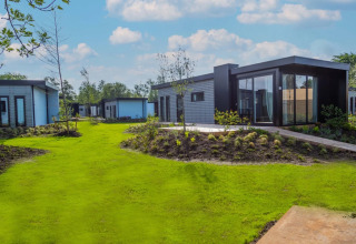 Cabañas modernas de glamping en un parque vacacional, rodeadas de césped verde y jardines cuidados.