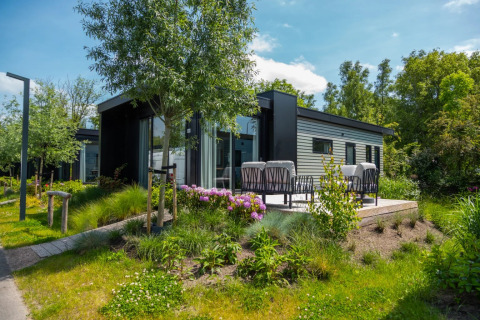 Cabaña glamping moderna en parque vacacional, rodeada de jardín, flores y área de asientos al aire libre.