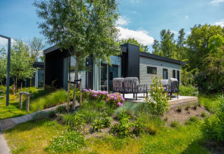 Cabane de glamping moderne dans un parc de vacances, entourée de verdure, fleurs et coin salon extérieur.