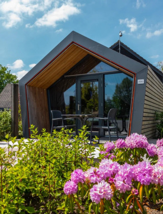 Moderne glamping lodge met grote ramen, omgeven door bloeiende bloemen in een vakantiepark.