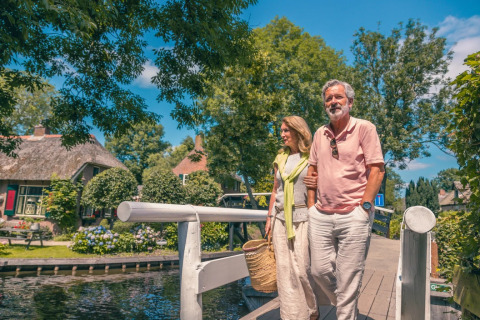 Couple âgé marchant main dans la main sur un pont dans un parc de vacances avec glamping et verdure.