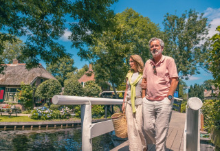 Älteres Paar spaziert entspannt über eine Brücke in einem Ferienpark mit Glamping und viel Natur.