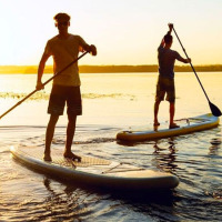 Two people stand-up paddleboarding on a lake at sunset, enjoying a holiday at a glamping park.