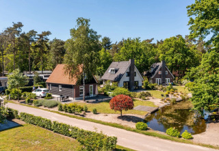 Parc de vacances avec hébergements glamping, cottages confortables, arbres et étang sous un ciel bleu.