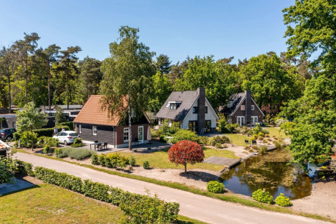 Vakantiepark met glamping accommodaties, charmante huisjes, bomen en een vijver op een zonnige dag.